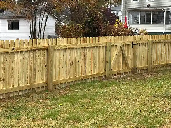 Wooden dog-ear privacy fence with a built-in gate on a residential lawn