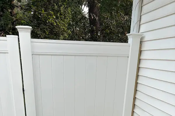Close-up view of a tall white vinyl privacy fence gate panel fitted snugly against white house siding.