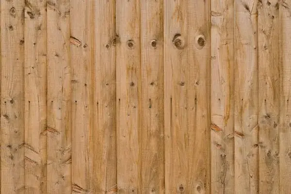 A full-frame view of light-toned vertical wood planks forming a wooden fence. The texture displays natural wood grains, several dark knots, and a horizontal line of small nail heads securing the boards.